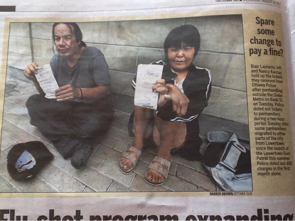 Two homeless on the sidewalk holding a fine they have been issued